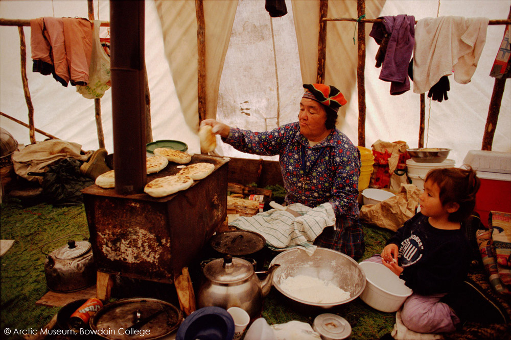 In a tent at an Innu hunting camp, Enen makes bannock on a wood stove. Southern Labrador, Canada. 1997
