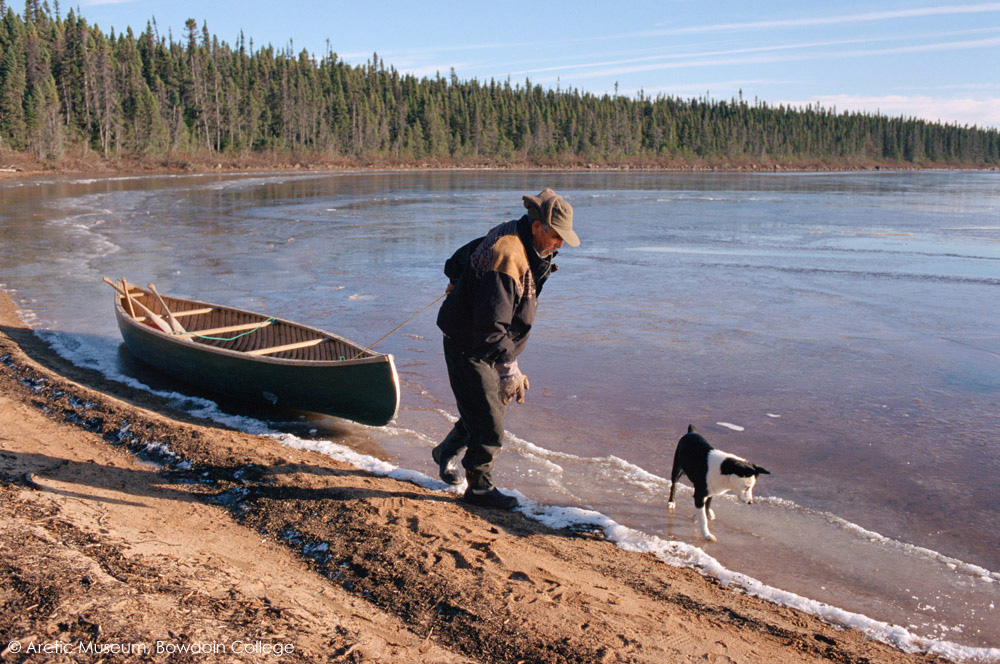 Uniam, an Innu hunter, hauls his canoe along the edge of a freezing lake in the autumn. Labrador, Canada. 1997