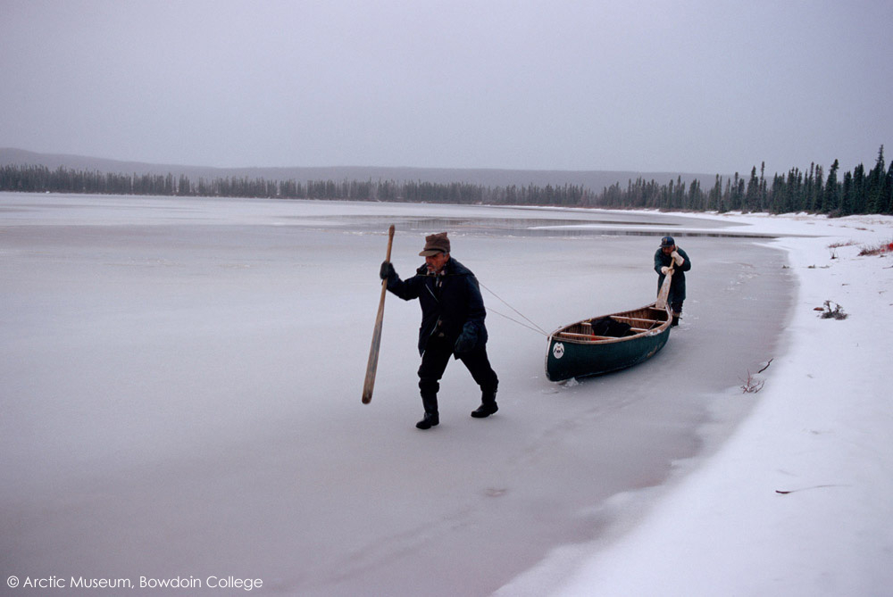 Two Innu hunters haul their canoe along the edge of a frozen lake. Labrador, Canada. 1997