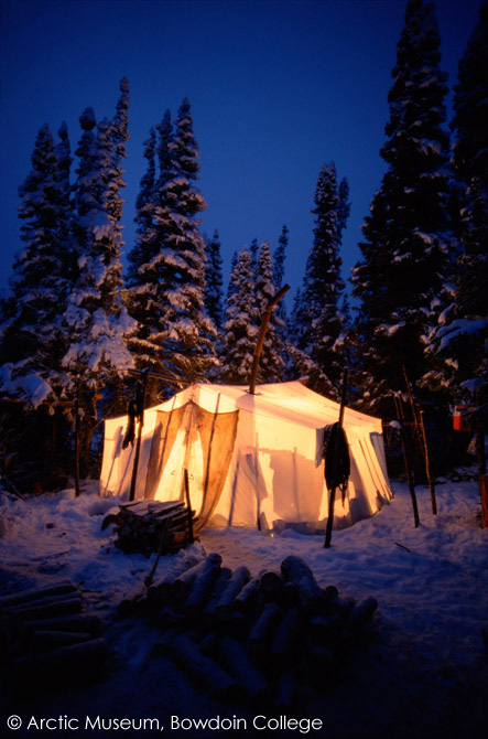 At dusk in boreal forest, light shines through a tent at an Innu autumn hunting camp. Southern Labrador, Canada. 1997