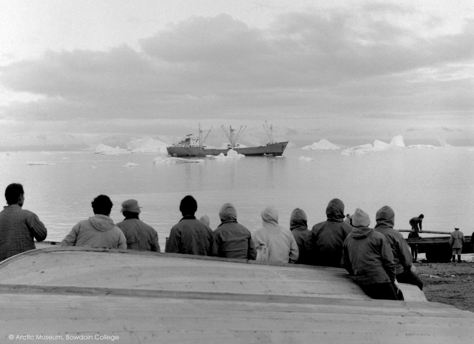 Inuit men stand on the beach as the year's first supply ship arrives at Qaanaaq. Thule, Northwest Greenland. 1971