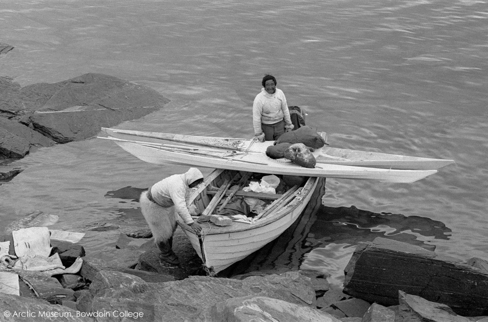 Agpalinguaq Angina, standing at the back of his boat, loaded with two kayaks, as he and another hunter are about to set off on a Narwhal hunt near Qeqertat. Inglefield Bredning, Thule, Northwest Greenland. (1977)